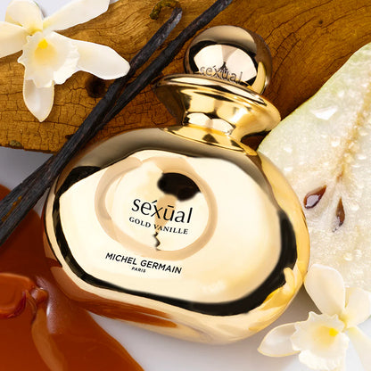 Gold and white perfume bottle labeled 'sexual GOLD VANILLE' by Michel Germain on a decorative background with flowers and wood.